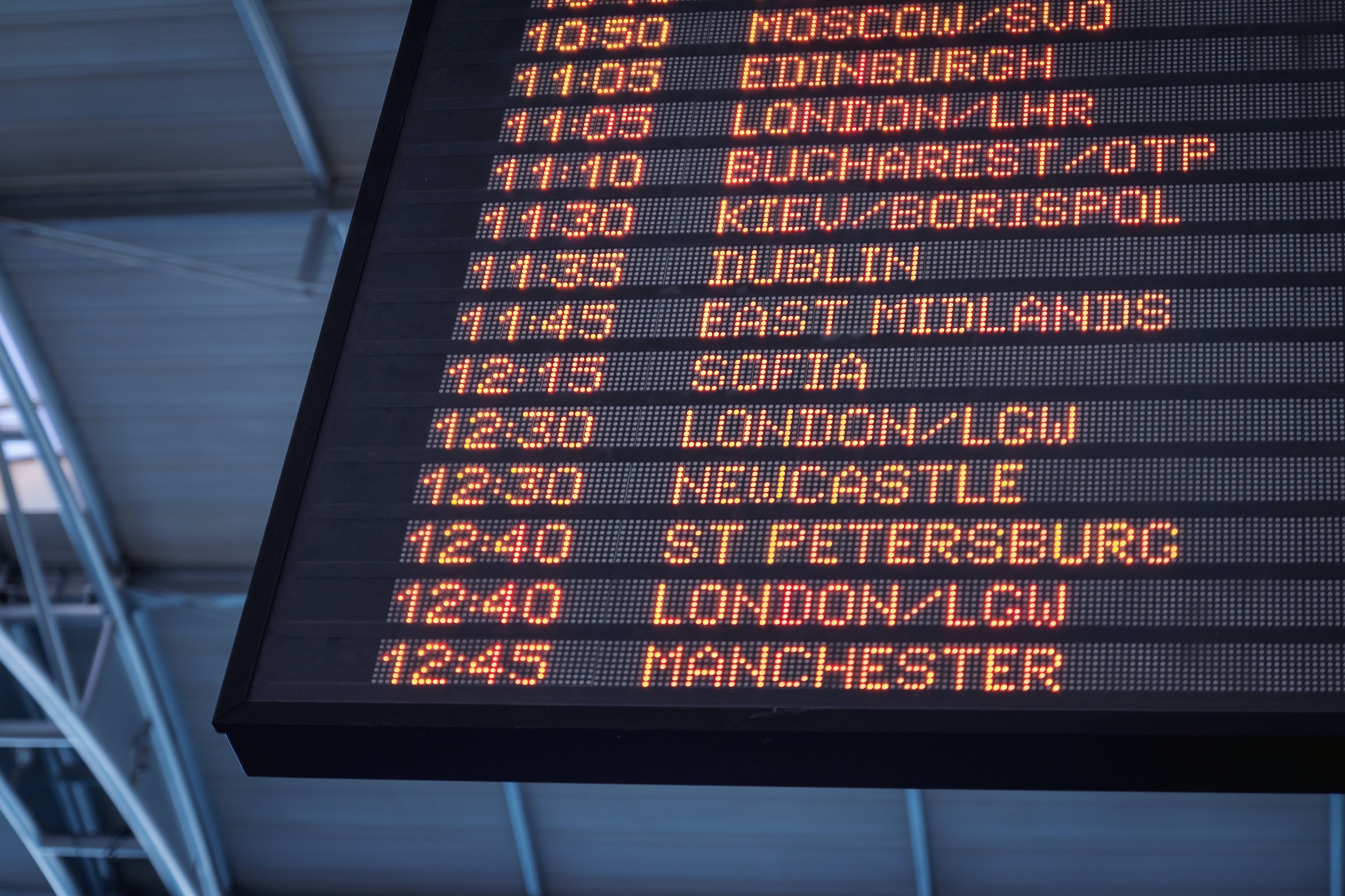 A departure board with orange LEDs on black. It shows a list of cities with departure times.
